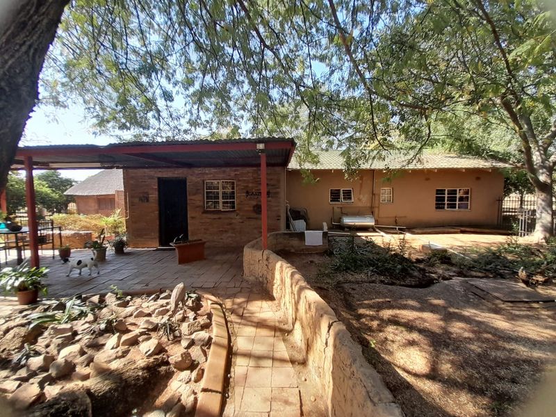 Rear view of the property featuring a covered patio area, brick and plaster exterior walls, and a stone retaining wall leading to the garden.