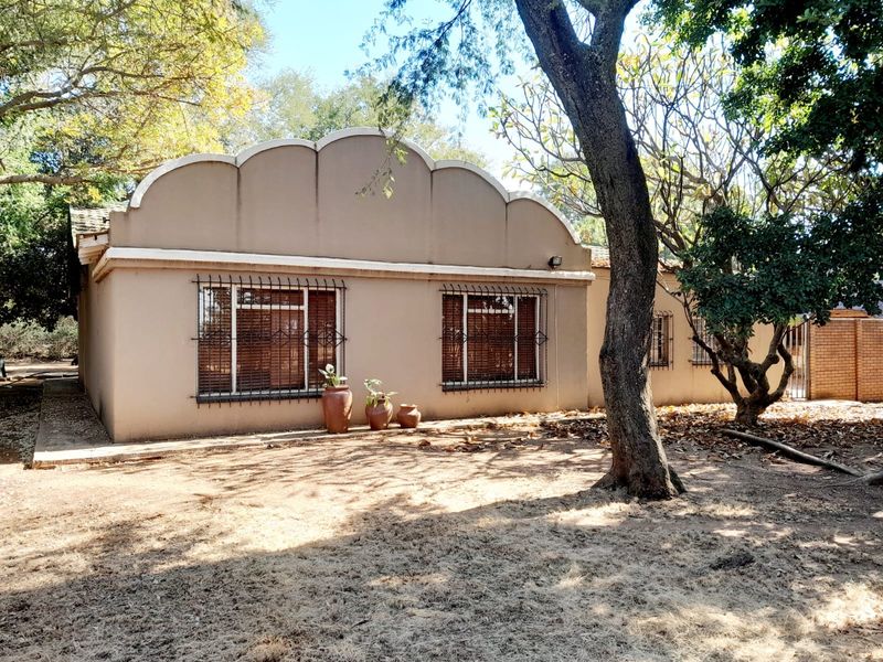 Rear elevation of the property featuring a distinctive scalloped parapet wall, security burglar bars on windows, and mature trees in a garden setting.