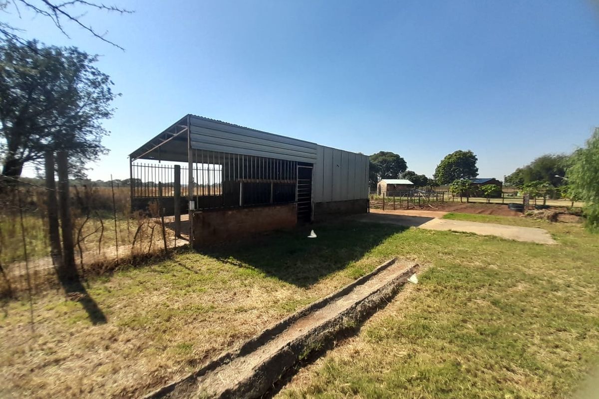 An outdoor agricultural structure featuring a corrugated metal shed with a brick base and a concrete feeding trough in a rural setting.