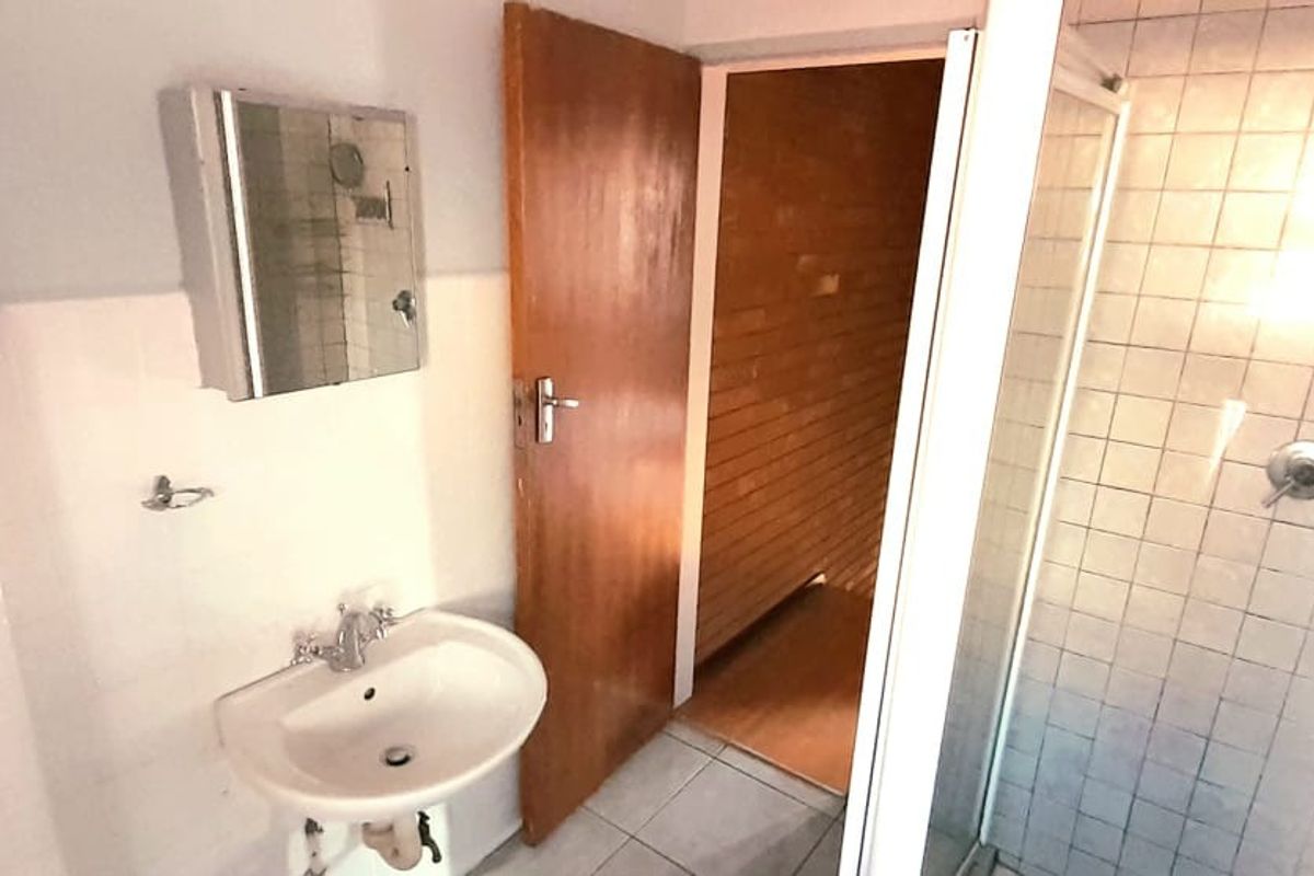 A functional bathroom featuring a shower enclosure, pedestal basin, and wall-mounted medicine cabinet with tiled walls and flooring.