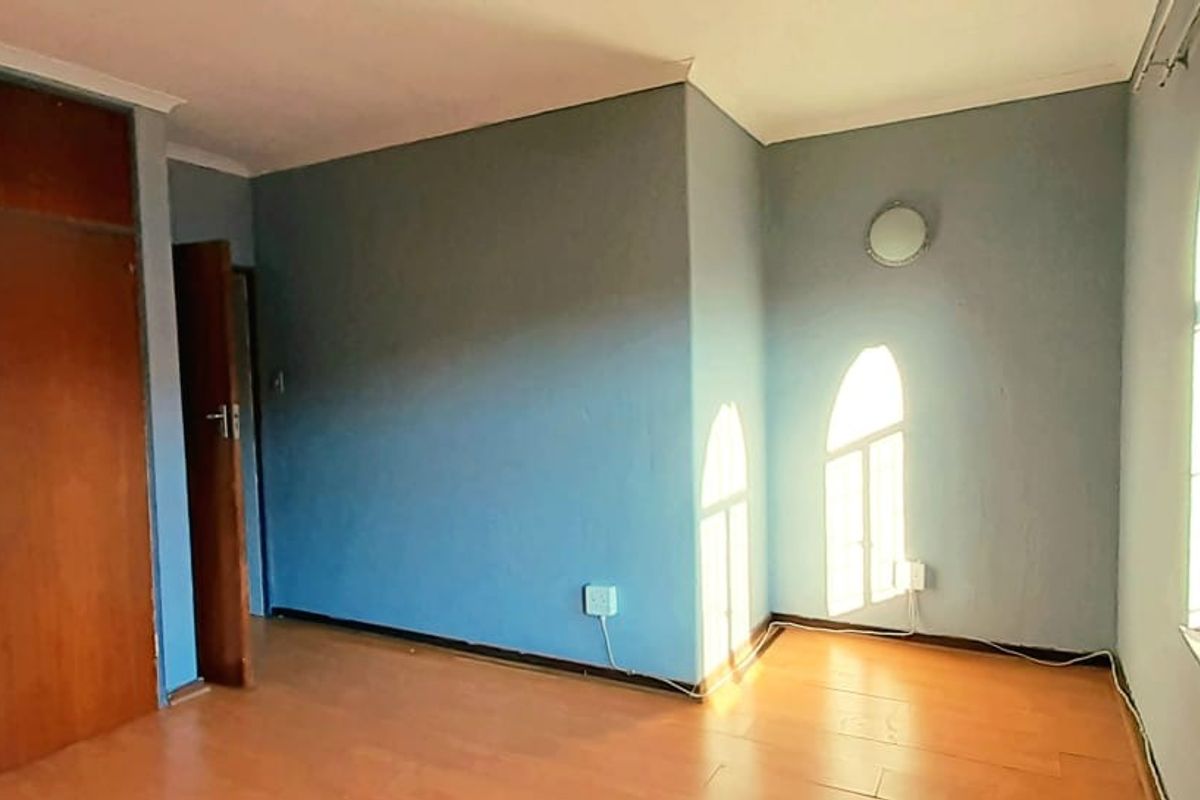 A bedroom featuring built-in wooden cupboards, laminate flooring, and arched windows allowing natural light.