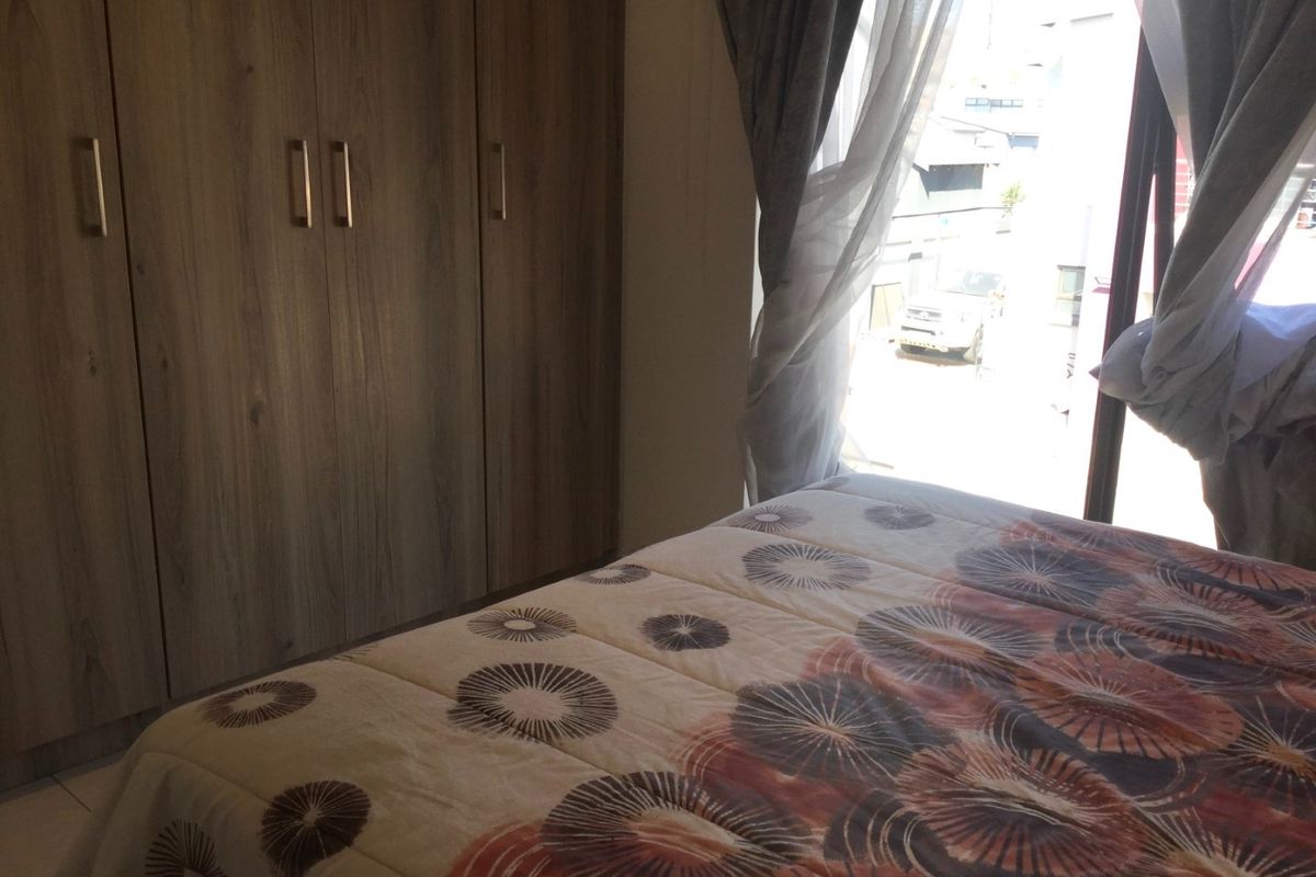 A bedroom featuring built-in wooden wardrobes and large windows allowing natural light, providing a functional and comfortable living space.