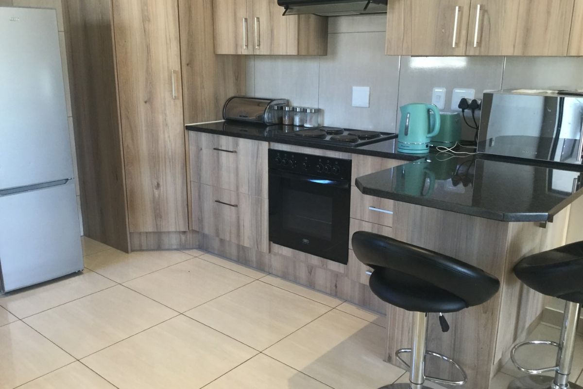 Modern kitchen featuring wood-grain cabinetry, dark granite countertops, built-in oven, hob, and extractor fan with tiled flooring.