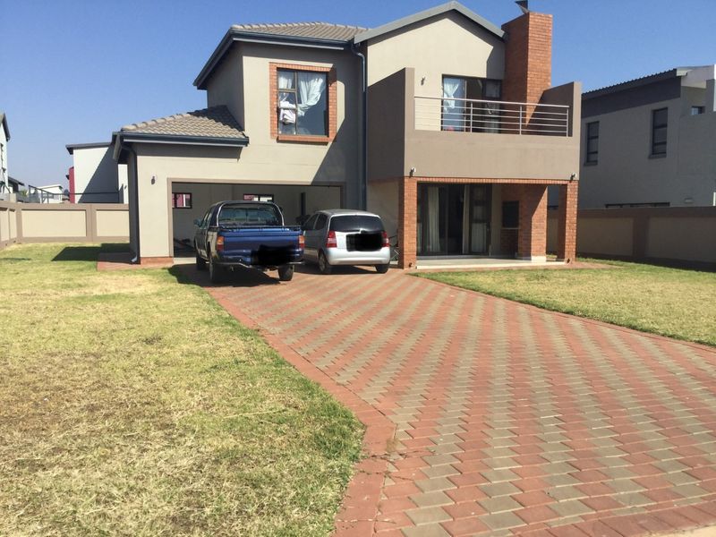 A double-story residential home featuring a paved driveway, double garage, and an upper-level balcony with brick accents.