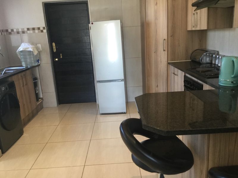 A functional kitchen featuring wood-finish cabinetry, dark granite countertops, tiled flooring, and a built-in hob with an extractor fan.