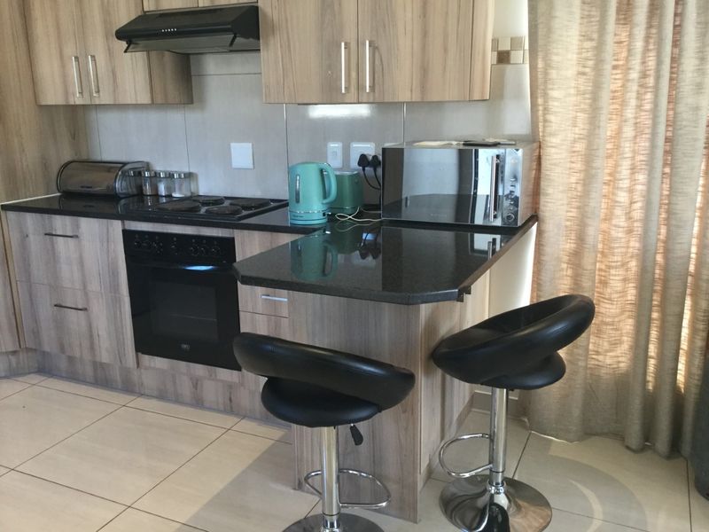 Modern kitchen featuring wood-finish cabinetry, granite countertops, built-in oven, hob, and extractor fan with a convenient breakfast nook.