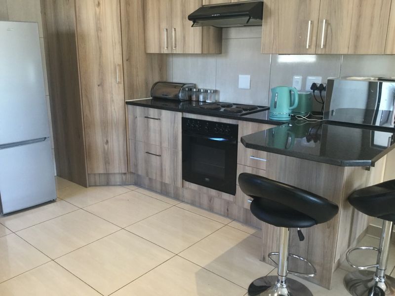 Modern kitchen featuring wood-look cabinetry, granite countertops, built-in oven and hob, extractor fan, and neutral tiled flooring.
