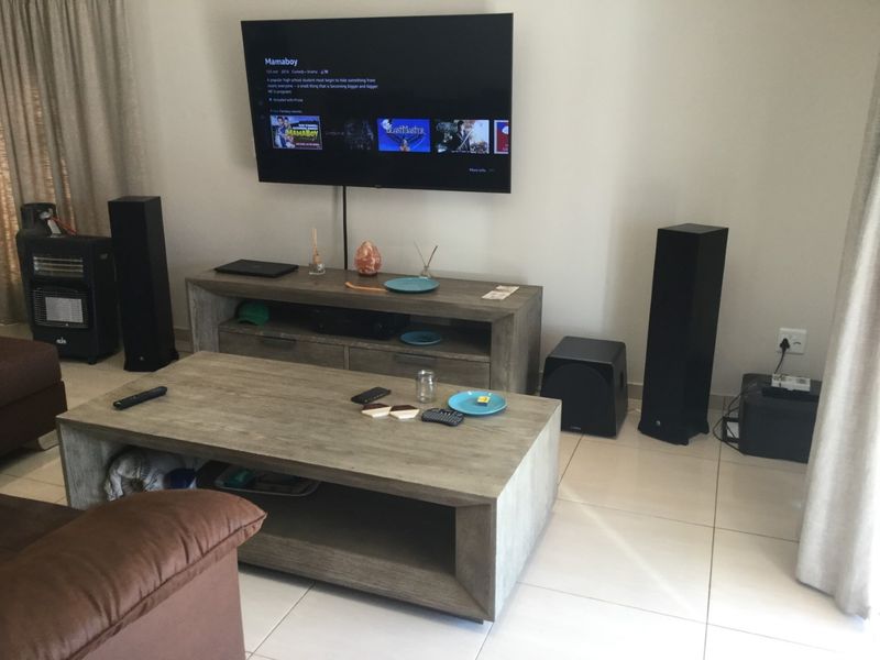 A living room featuring neutral tiled flooring and a wall-mounted television setup.