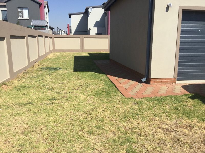 A rear garden area featuring a paved walkway, boundary wall, and access to the garage.