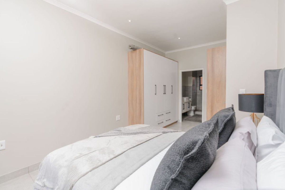 A modern bedroom featuring built-in wardrobes with a light wood finish and an en-suite bathroom entrance.