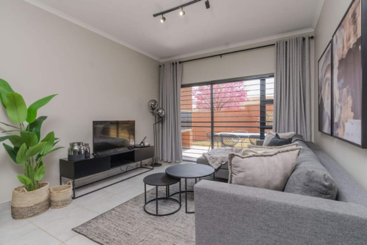 A bright and modern living room featuring large sliding glass doors that open to an outdoor patio area, finished with neutral tiled flooring.