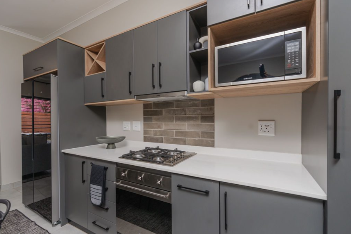 Modern kitchen featuring sleek grey cabinetry, light stone countertops, a built-in gas hob, oven, and integrated microwave with a stylish subway tile backsplash.