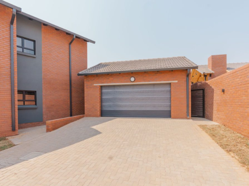 Front view of a modern townhouse featuring a face-brick facade, a paved driveway, and a secure automated garage.