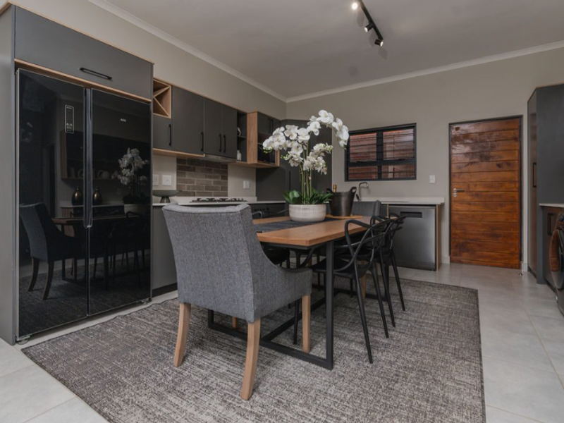 Modern open-plan kitchen and dining area featuring sleek dark cabinetry, integrated appliances, tiled flooring, and contemporary track lighting.