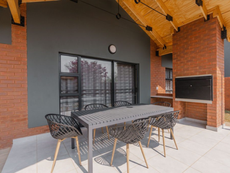 Covered patio featuring exposed timber roof trusses, tiled flooring, and a built-in braai, providing an ideal space for outdoor entertaining.