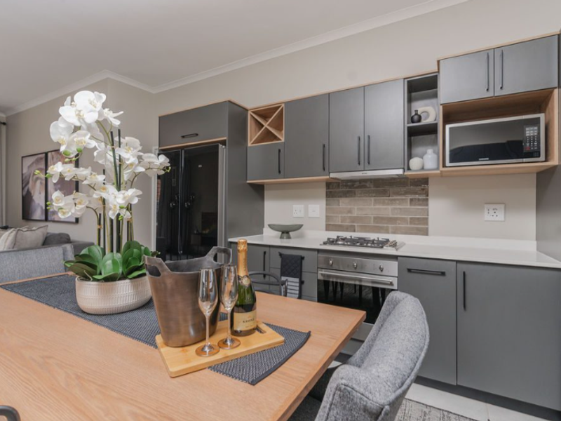 Modern open-plan kitchen featuring sleek grey cabinetry, stone countertops, integrated appliances, and a stylish tiled backsplash, seamlessly flowing into the dining area.
