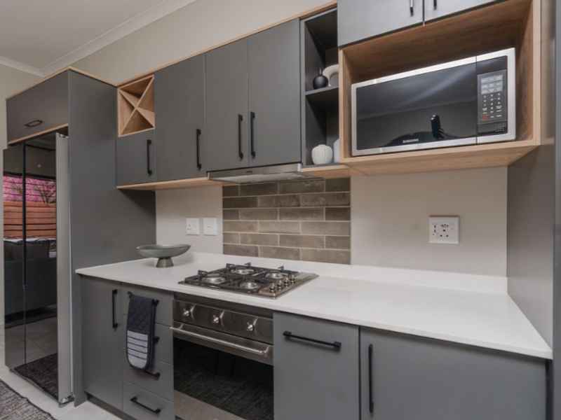 Modern kitchen featuring sleek grey cabinetry, stone countertops, a gas hob, built-in oven, and integrated microwave with a stylish tiled backsplash.