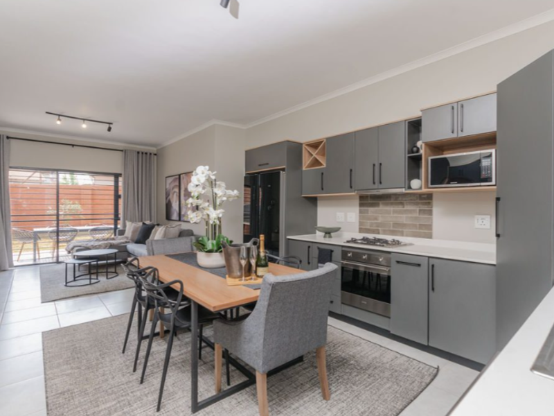 Modern open-plan living area featuring a sleek kitchen with built-in appliances, stone countertops, and seamless flow to the outdoor patio through sliding glass doors.