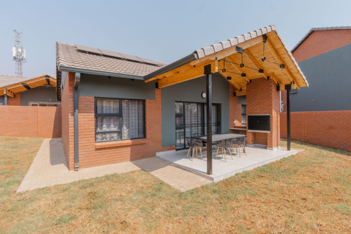 Rear view of a modern townhouse featuring a covered patio with a built-in braai, exposed timber trusses, and a private garden area.