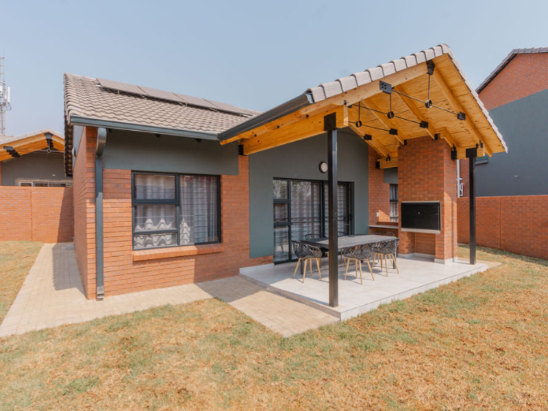 Rear view of a modern townhouse featuring a covered patio with a built-in braai, exposed timber trusses, and a private garden area.