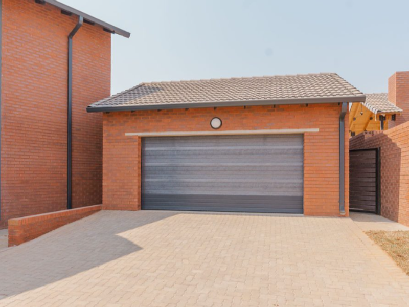 A well-maintained brick townhouse garage featuring a modern sectional door and a paved driveway.