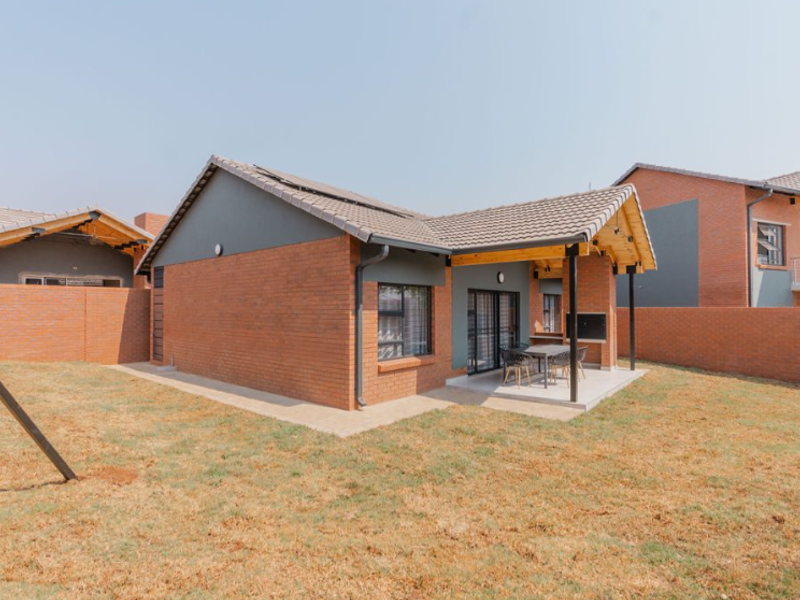Rear view of the townhouse featuring a brick facade, tiled roof, and a covered patio area with a built-in braai.