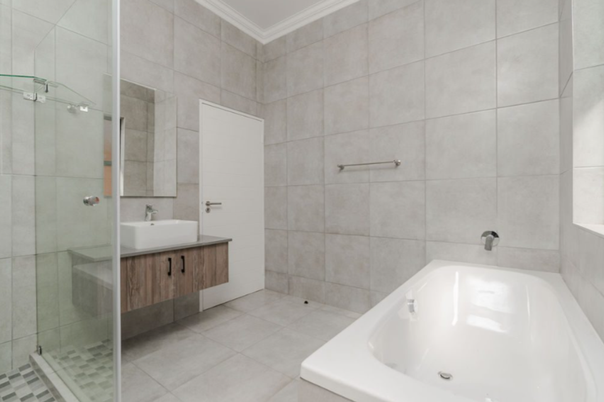 Modern bathroom featuring a glass-enclosed shower, a floating vanity with a vessel sink, and a built-in bathtub with neutral wall and floor tiling.