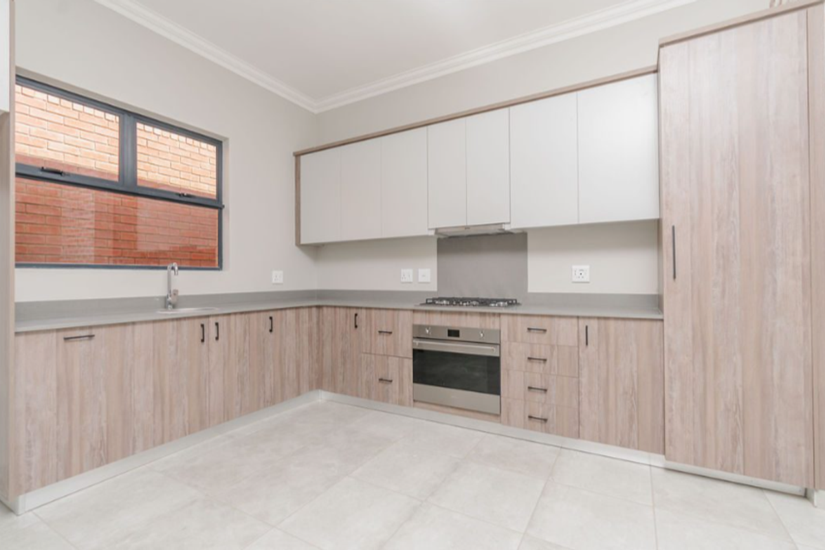 Modern kitchen featuring light wood-grain cabinetry, stone countertops, built-in oven, gas hob, extractor fan, and tiled flooring.