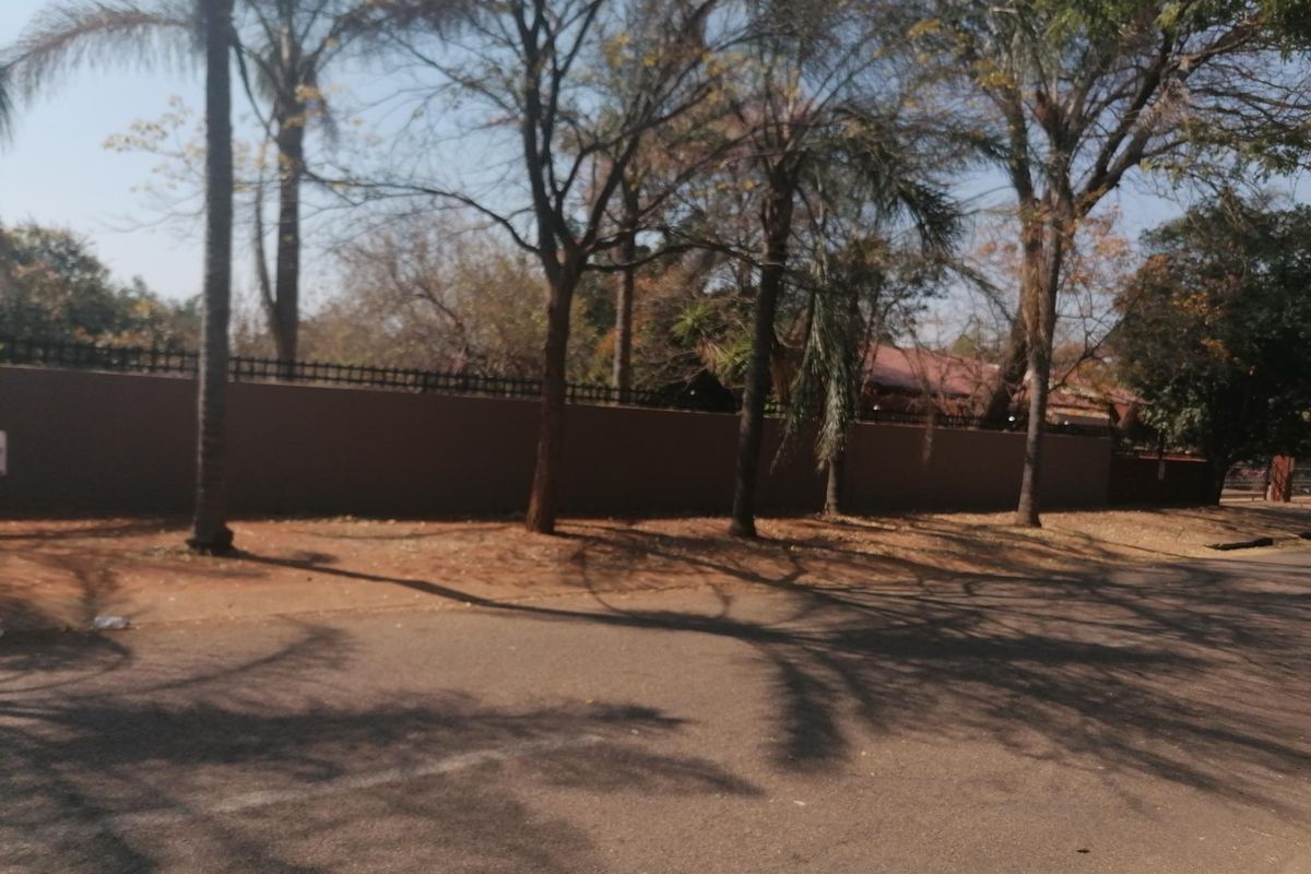 Street view of the property showing a solid perimeter wall with integrated security fencing and mature trees along the boundary.
