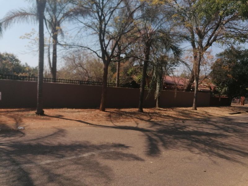 Street view of the property showing a solid perimeter wall with integrated security fencing and mature trees along the boundary.