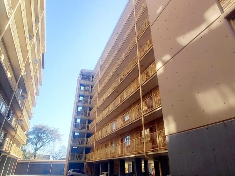 Exterior view of a multi-story apartment complex featuring brick and concrete facades with multiple balconies and a ground-level covered parking area.