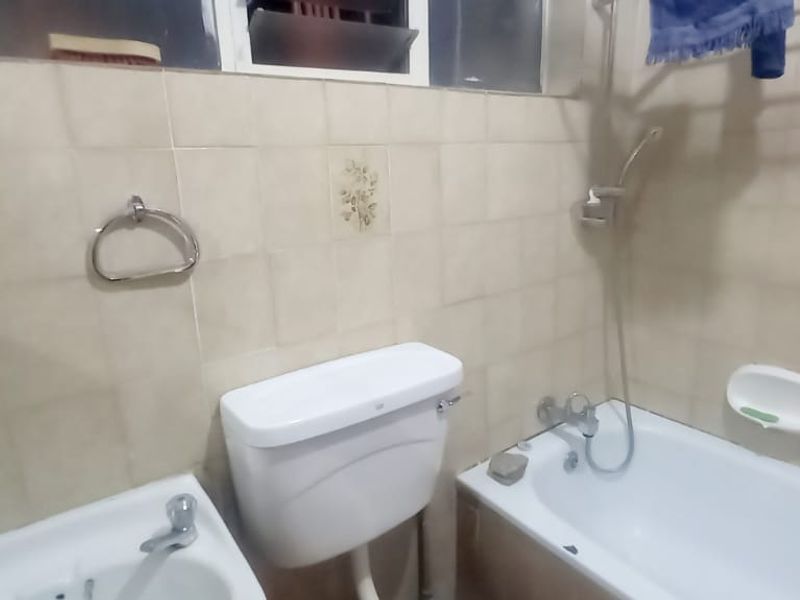 A dated bathroom featuring a standard bathtub, wall-mounted shower, and toilet with ceramic wall tiling throughout.