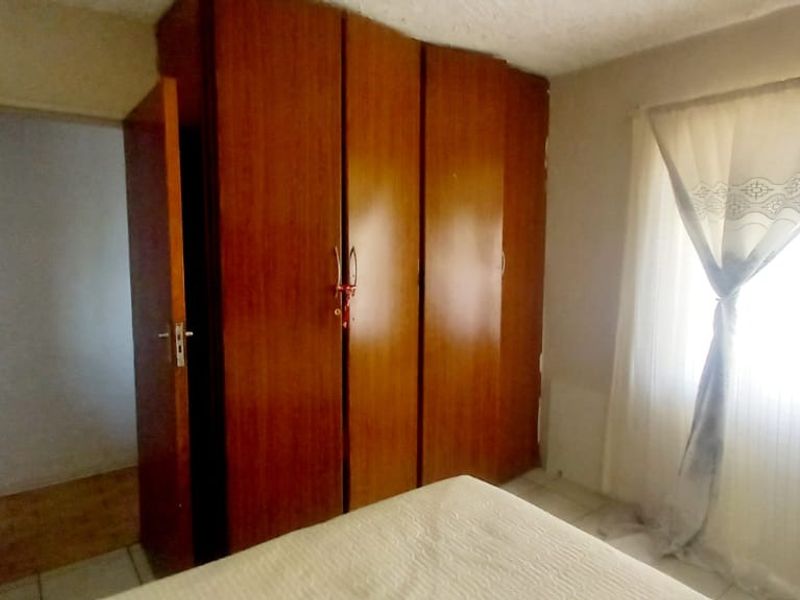 A bedroom featuring a large built-in wooden wardrobe and tiled flooring, offering a functional space with potential for modern updates.