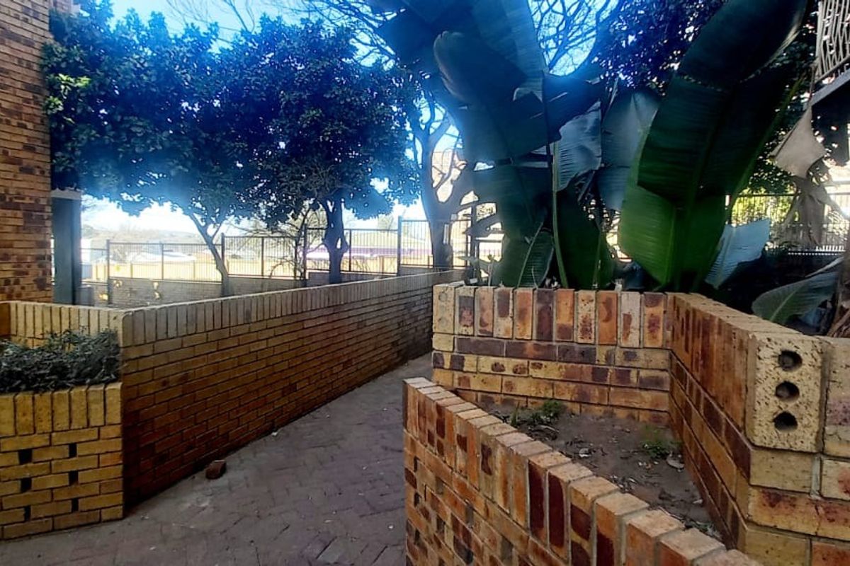 A rear exterior area featuring brick planter boxes, a paved walkway, and established boundary fencing.