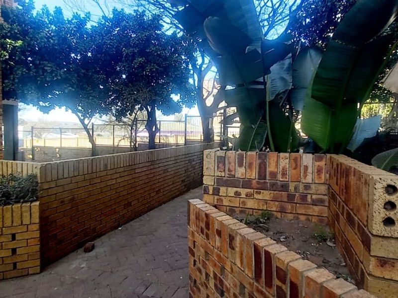 A rear exterior area featuring brick planter boxes, a paved walkway, and established boundary fencing.
