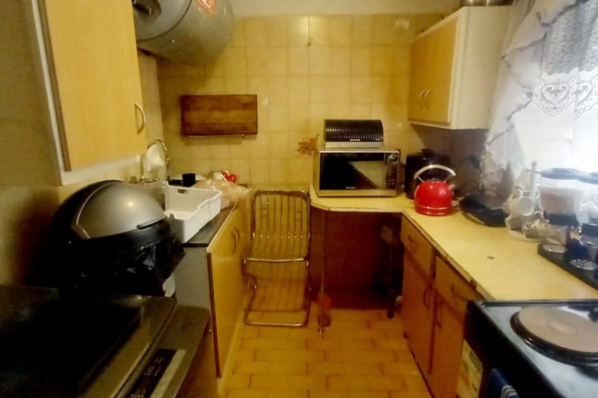 A compact, dated kitchen featuring tiled walls and floors, built-in cabinetry, and an electric stove, offering potential for a modern renovation.