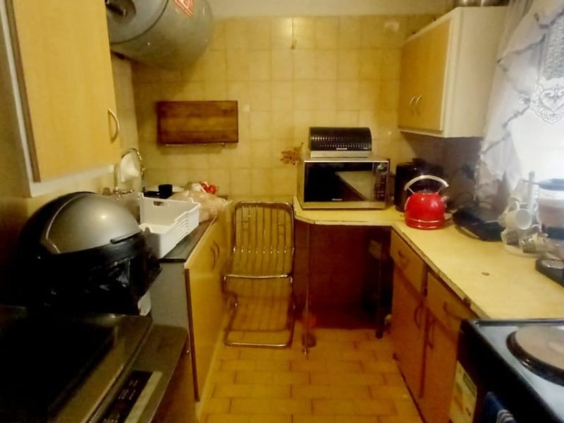 A compact, dated kitchen featuring tiled walls and floors, built-in cabinetry, and an electric stove, offering potential for a modern renovation.