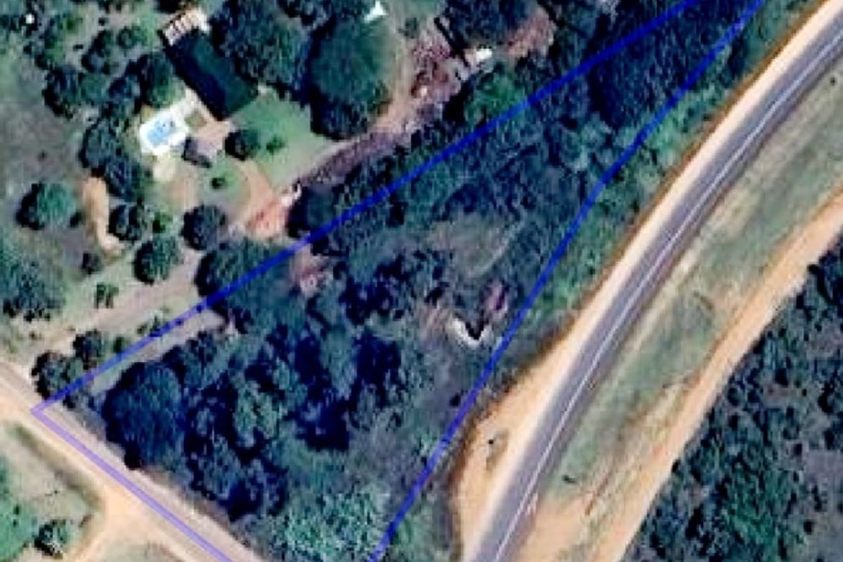 Aerial view of a vacant residential plot with established trees, showing its triangular shape and proximity to the adjacent road.