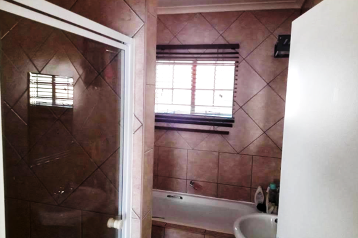 A functional bathroom featuring a built-in bathtub, a separate shower enclosure with a white frame, and a wall-mounted basin.