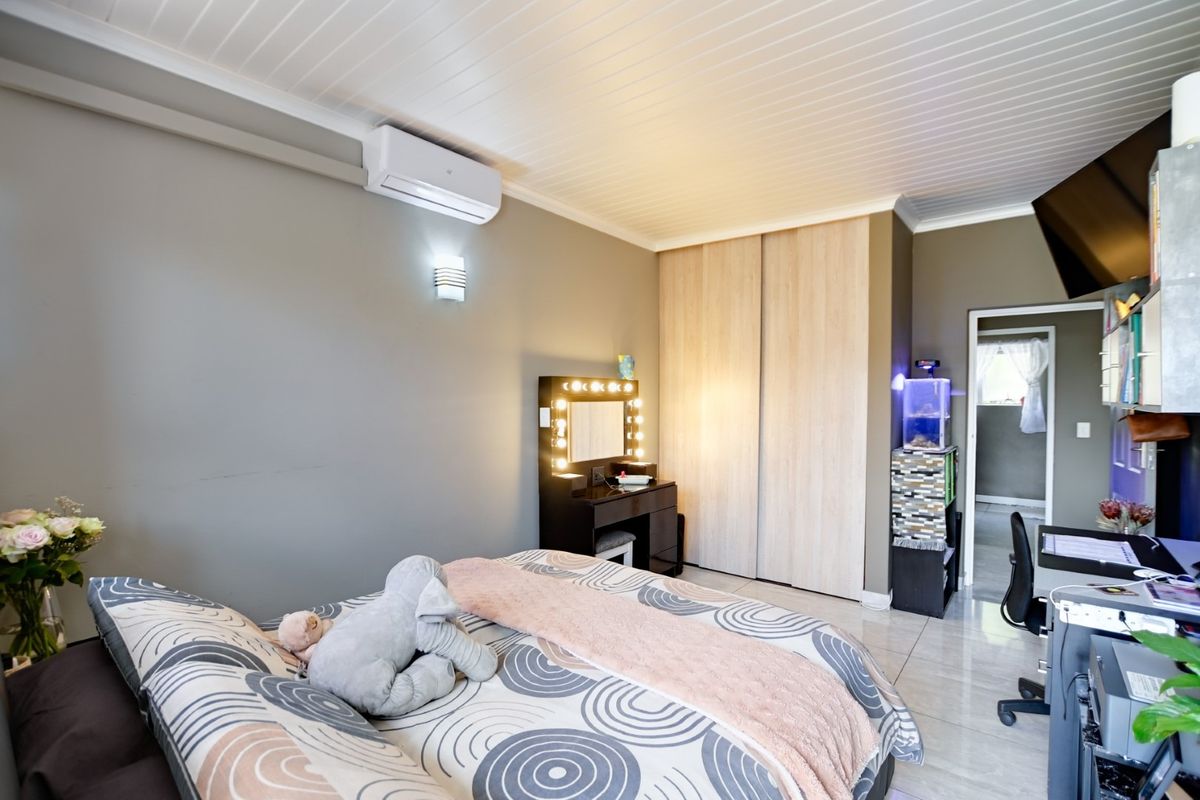 A well-maintained bedroom featuring built-in wooden wardrobes, tiled flooring, a wall-mounted air conditioning unit, and a tongue-and-groove ceiling finish.