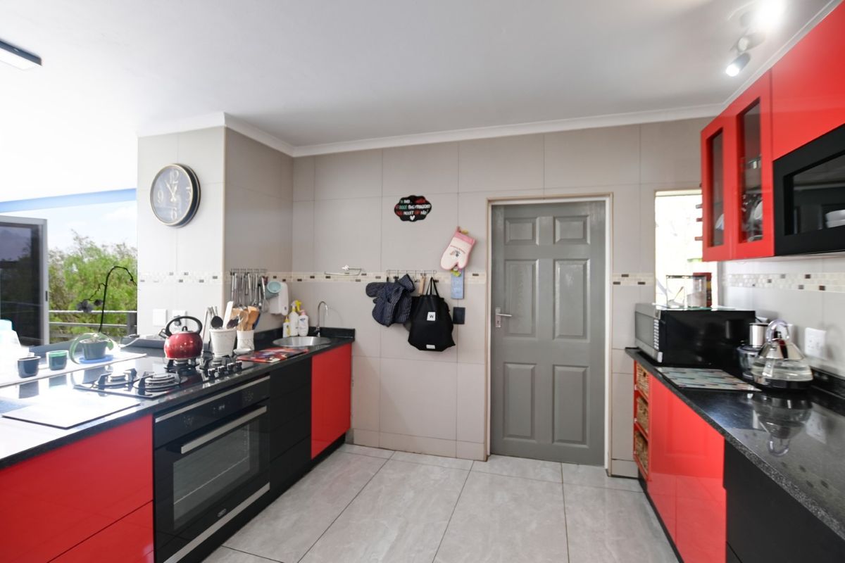 Modern kitchen featuring high-gloss red and black cabinetry, granite countertops, built-in oven, gas hob, and tiled flooring.