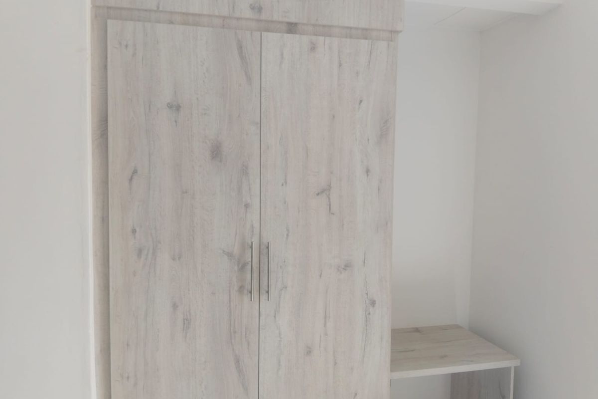 A built-in wardrobe with a light wood-grain finish and an integrated desk or vanity surface, providing functional storage and workspace in the bedroom.