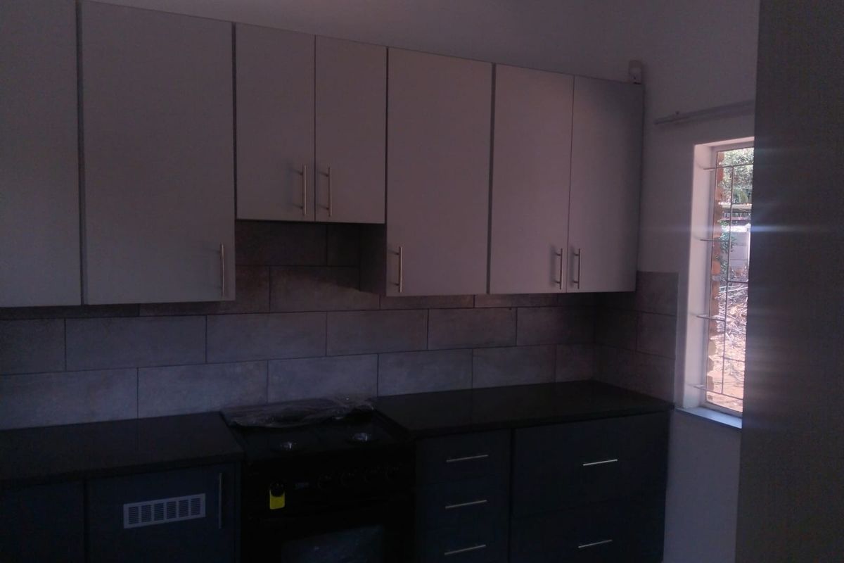 A modern kitchen featuring dark cabinetry, contrasting light upper cabinets, stone-look tiled backsplash, and a built-in oven and hob.