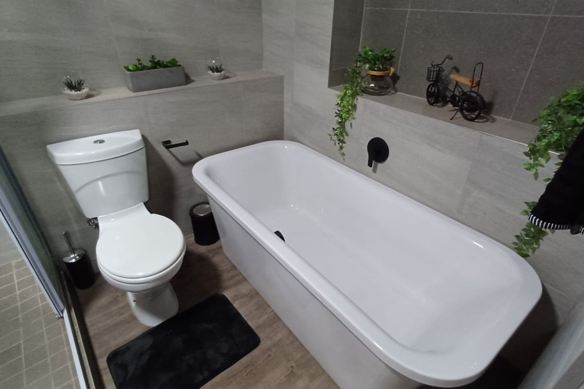 Modern bathroom featuring a white bathtub, a close-coupled toilet, and neutral wall tiling with a built-in recessed shelf.