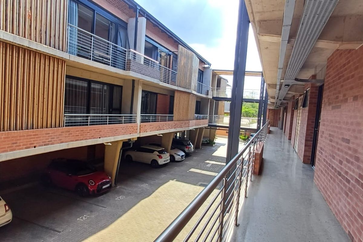 An elevated walkway overlooking a covered parking area within a modern apartment complex featuring exposed brickwork and timber slat architectural detailing.