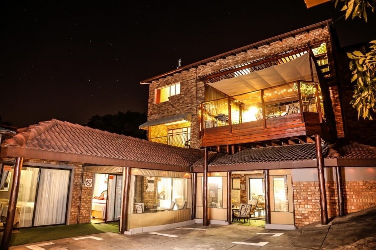 Night view of a multi-level residential property featuring exposed brickwork, a raised wooden balcony, and a covered patio area.