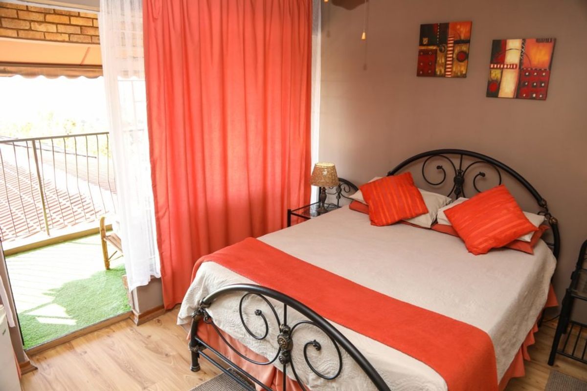A cozy bedroom featuring laminate flooring and direct access to a private balcony through a sliding glass door.