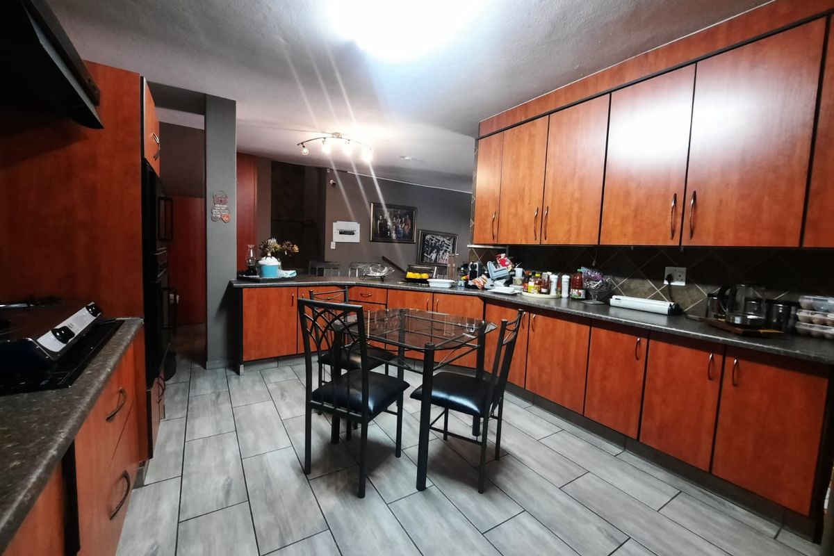 Spacious kitchen featuring extensive wood-tone cabinetry, dark countertops, tiled backsplash, and modern grey floor tiles, offering ample storage and workspace.