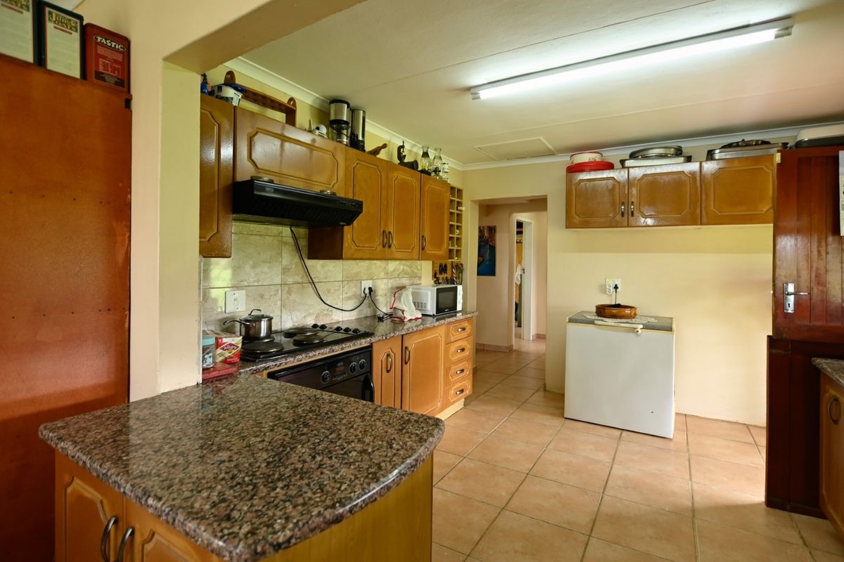 A functional kitchen featuring granite countertops, wooden cabinetry, built-in oven, and ceramic hob, with tiled flooring and backsplash throughout.