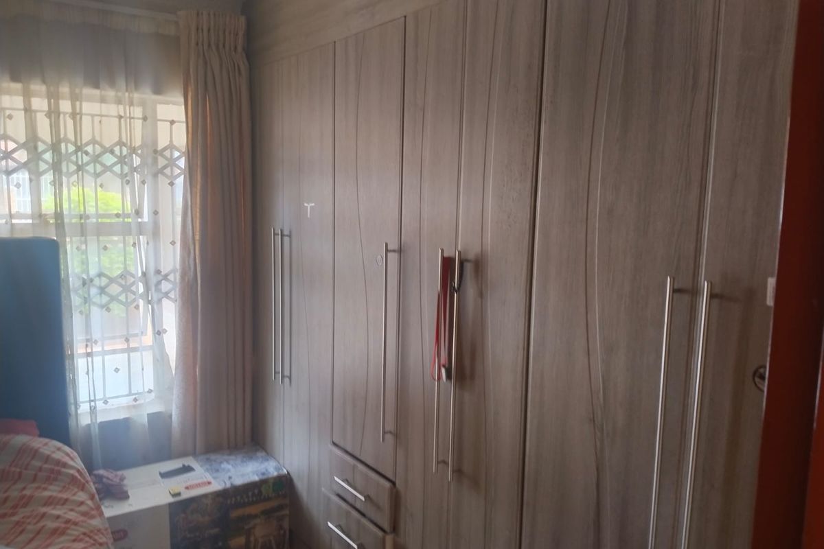 A bedroom featuring floor-to-ceiling built-in wooden cabinetry with modern metal handles and a window with security bars.